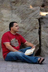 Man reading, leaning against stone wall.