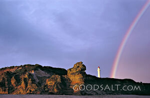 rock formation with rainbow and lighthouse