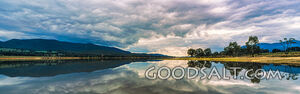 Shores and cloudy sky reflected in large lake waters.