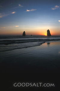 The sun setting on two large rocks in the middle of the ocean.