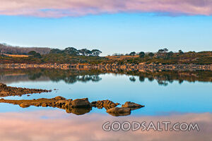 Sunrise over mirror water and rocks of alpine lake.