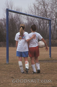 Two girls from different teams, walking together on soccer field 
