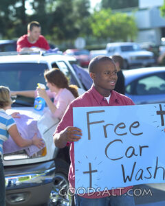 Teenagers washing cars while another boy holds up a "Free Car Wash" sign.