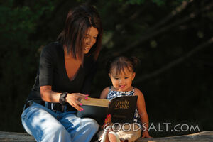 Woman reading Bible to little girl outdoors in summer.