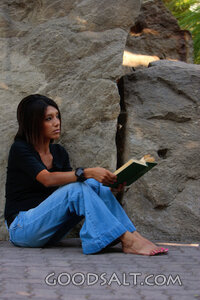 Woman reading, leaning against stone wall.