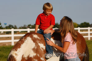 Woman smiling up at little boy on horseback.